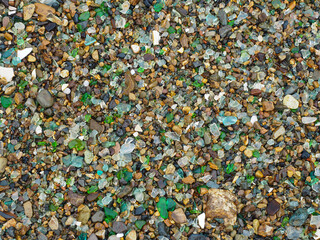 The texture of a stone beach with many pieces of colored glass turned by water.