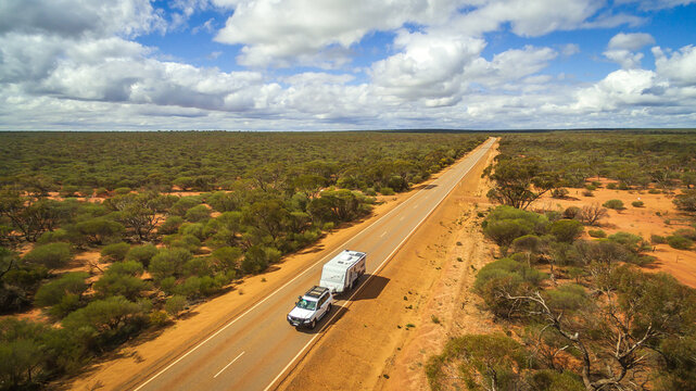 Aerial view of 4WD and modern caravan on an outback highway in Australia under a blue cloudy sky