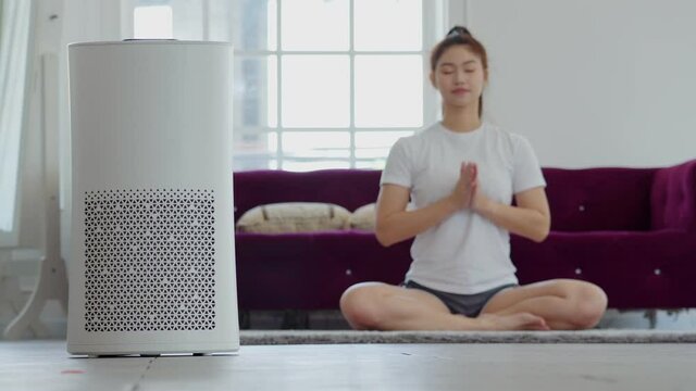 Air purifier in cozy white Living room for filter and cleaning removing dust PM2.5 HEPA at home with woman exercise yoga in background,for fresh air and healthy life,Air Pollution Concept