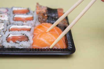 Close up of chopsticks picking salmon niguiri from black plastic tray.