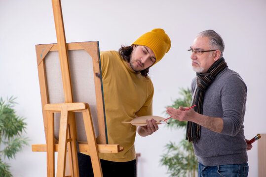 Old man taking lesson from young painter