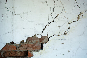 An old brick wall with peeling plaster and many cracks