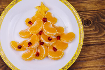 Christmas tree made of mandarin lobules and pomegranate on wooden table. Top view. Creative idea for Christmas and New Year festive desserts. Funny food idea for kids
