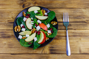 Autumn spinach salad with apple, feta cheese, walnut and dried cranberry on wooden table. Top view. Healthy vegetarian food
