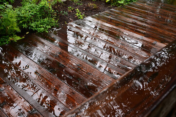 雨に濡れた木製の手すりと木の床の水に映る樹木のシルエット