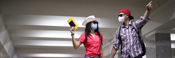 Happy couple in protective medical mask go tunnel on arport terminal and hold passport in hand portrait. Travel after covid 19 concept