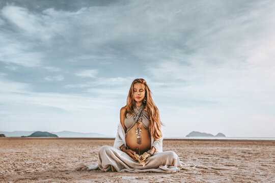 beautiful young stylish pregnant woman with boho accessories on the beach at sunset