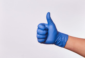 Mano de hombre levantando el pulgar con guantes de nitrilo en fondo blanco. Seña de afirmación...