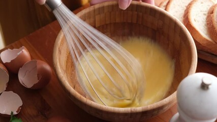 Whisking eggs in wooden bowl with metal wire whisk. Cooking breakfast