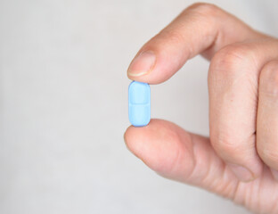 Blue pill sandwiched between thumb and forefinger