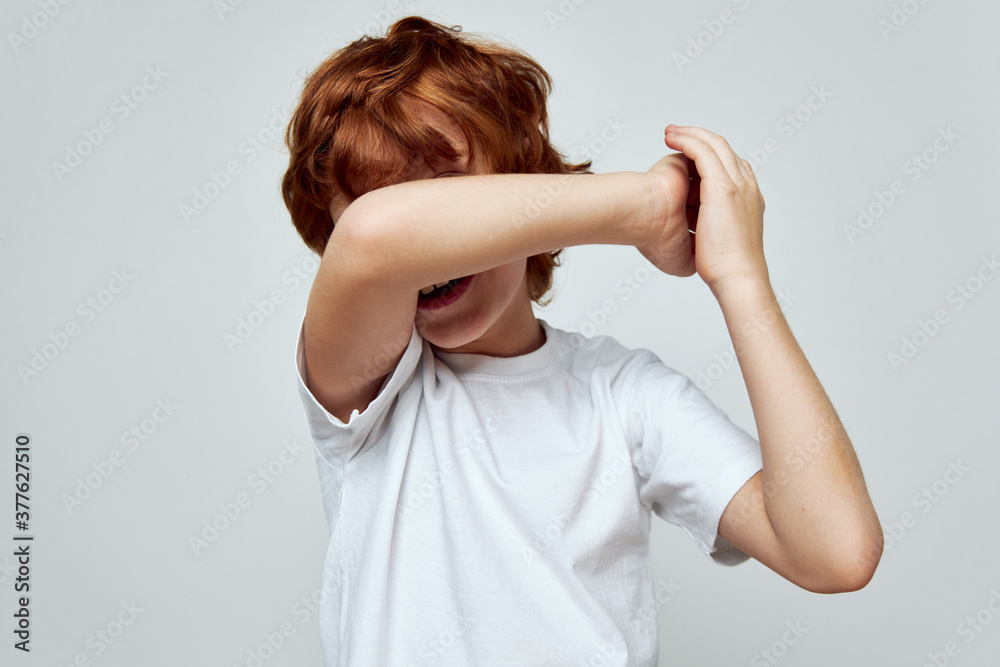 Wall mural redhead boy covers hand over face white t-shirt cropped view studio 