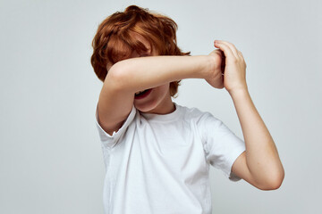 redhead boy covers hand over face white t-shirt cropped view studio  - obrazy, fototapety, plakaty