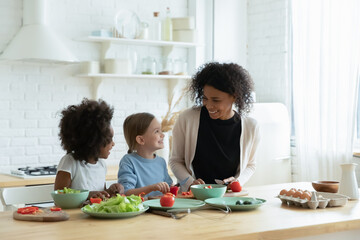 Funny small cute multiracial children girls enjoying cooking master class from affectionate loving...