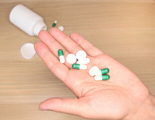 Several pills in the palm from a jar overturned on the table below