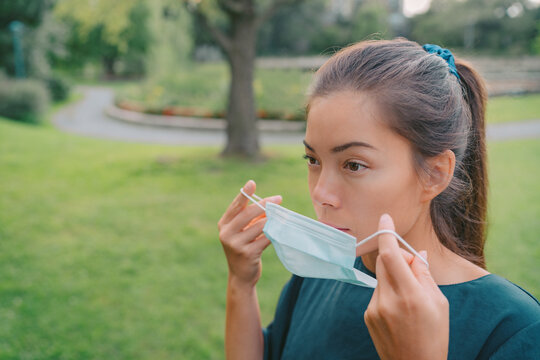 Woman putting on a surgical face mask for mandatory wearing in city. Serious Asian girl using medical grade covering.