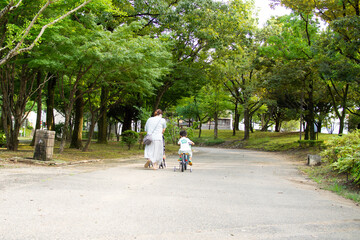 公園を自転車とベビーカーで散歩する日本人の親子