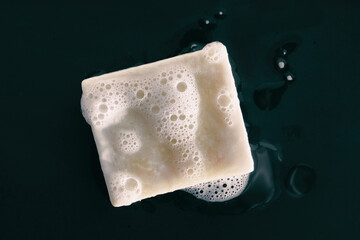 Soap bar natural diy olive oil foaming with foam bubbles texture on black background .Top view....