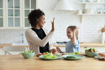 Happy african ethnicity mother giving high five to joyful adorable european adopted kid daughter,...