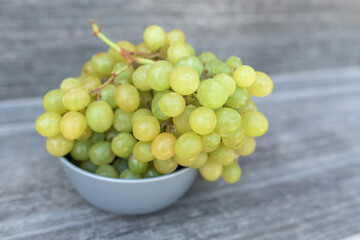 A bunch of ripe green grapes in a gray plat on a gray background.