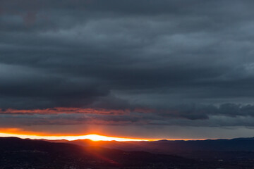 Sunset over mountains and valley, with sun coming down through an hole in the clouds