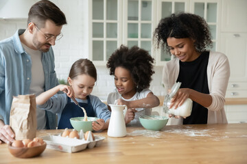 Happy interested multiethnic small children girls in aprons involved in preparing dough for homemade pastry with affectionate loving african american mommy and european father in modern kitchen....