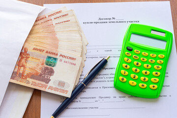 On the table is a contract for the sale of a land plot, a bundle of money in an envelope, a pen and...