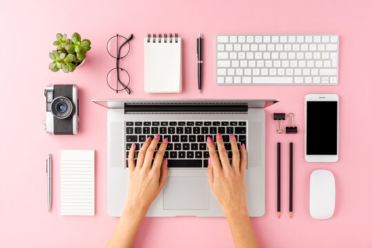 Female hands working on modern laptop on pink background with accessories. Office desktop. Flat lay