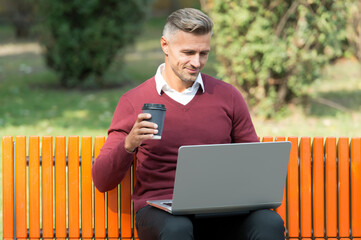 Fototapeta premium nice start of the day. good morning. mature handsome man work on computer outdoor. well groomed man sit on bench with coffee. confident businessman is online. casual business fashion. agile business