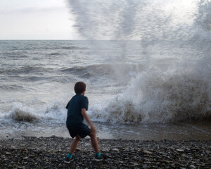 Boy on the seashore scared and running away from storm waves.