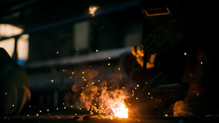 Arc welder with welding mask and orange sparks.
