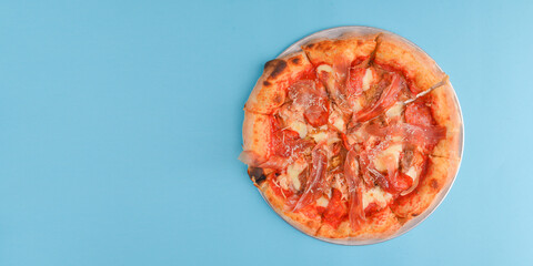 Whole Italian pizza with cheese and mushrooms on a metal tray over bright blue pastel bakcground.