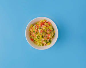 Fresh vegetables and green salad served in a bowl over pastel blue background. Healthy eating concept.