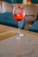 Red cocktail with ice served in a glass on wooden table with blurred restaurant background. Refreshing summer beverage.