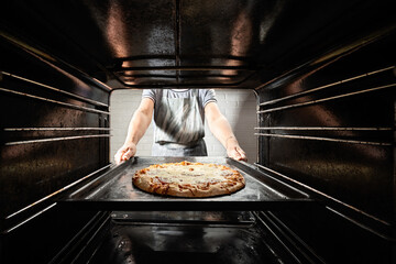 Chef prepares pizza in the oven, view from the inside of the oven