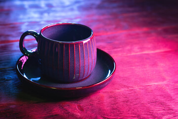 Coffee cup on the wooden table background in neon lights close up.