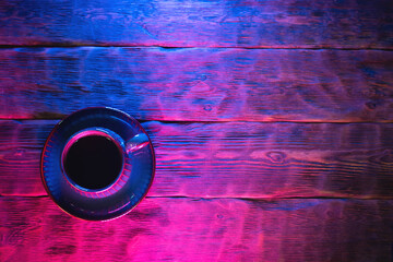Coffee cup on the wooden table background in neon lights.