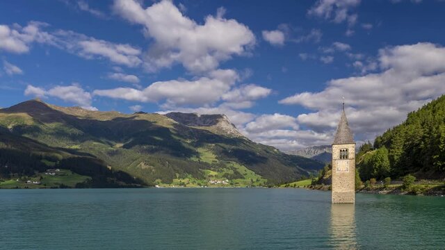 The top of the old bell tower of Curon (Graun) emerges from the waters of Lake Resia, against a dramatic sky, South Tyrol, Italy. Time lapse motion