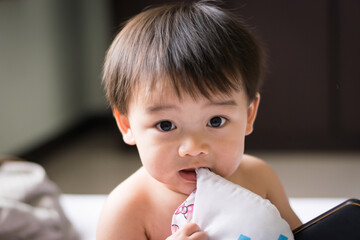 Little asian boy gnawing his pillow
