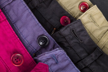 Fragment of four cotton twill pants red, blue, black, beige with open buttons.