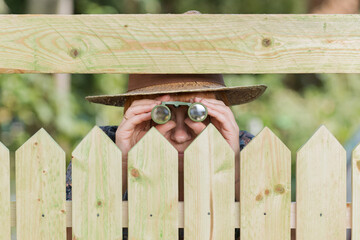 Fototapeta Curious neighbor stands behind a fence and watches with binoculars obraz