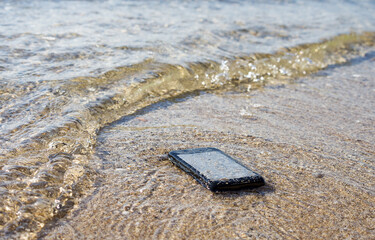 Lost smartphone on the seashore while on vacation. Repair of drowned mobile phones, concept image.