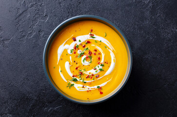 Butternut squash soup with cream in black bowl. Dark background. Top view.