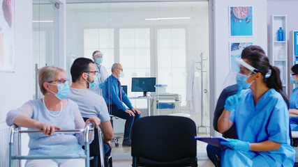 Fototapeta premium Doctor in examination room listening senior patient lungs with stethoscope. Medical staff visor against coronavirus in discussing with disabled senior womam in hospital waiting area.