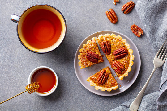 Pecan pie, tart slice on a plate with cup of tea. Grey background. Top view.