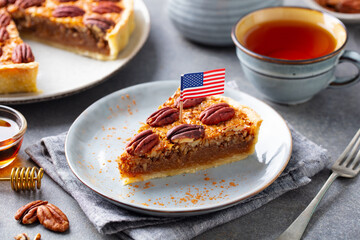 Pecan pie, tart slice on a plate with American flag with cup of tea. Gray background. Close up.