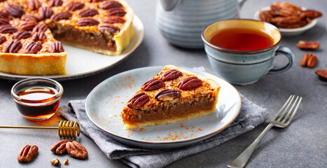Pecan pie, tart piece on a plate with cup of tea. Grey background. Close up.