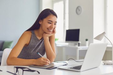 Happy young girl working on design project using modern graphic tablet and laptop computer