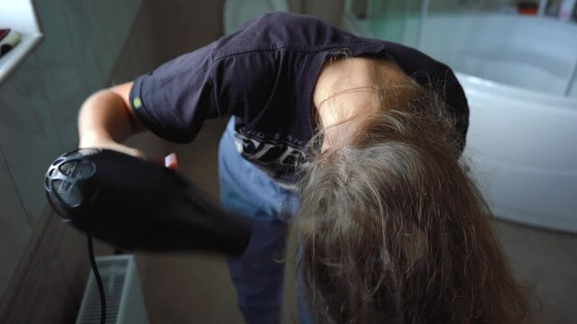 girl dries her hair with a hair dryer in the bathroom