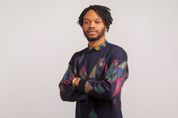 Concentrated african man with dreadlocks seriously and professionally looking at camera, assertiveness. Indoor studio shot isolated on gray background