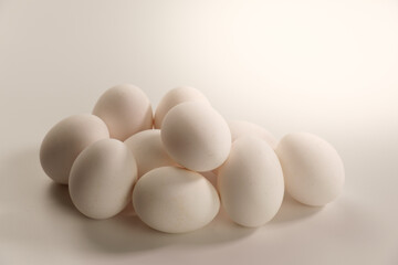 Weiße Eier gestapelt auf einem Haufen im warmen Gegenlicht auf einem neutralen warm-weißen...